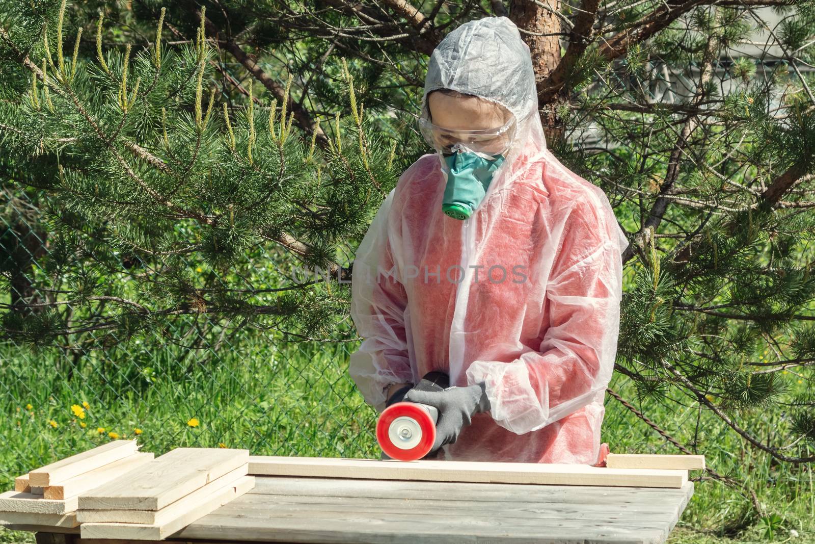 Woman carpenter in respirator, goggles and overalls handles a wooden board with a Angle grinder by galsand