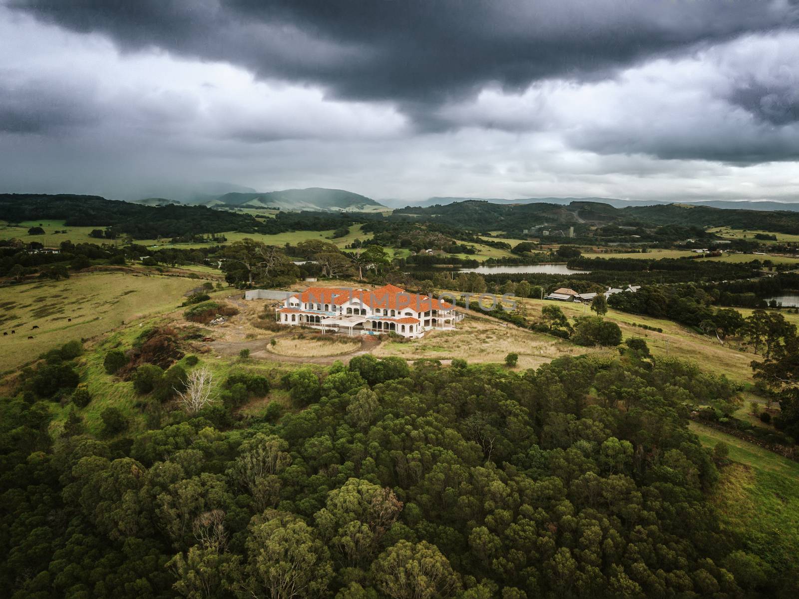 Storm clouds loom heavy over an abandoned mansion that now sits derelect in rural countryside
