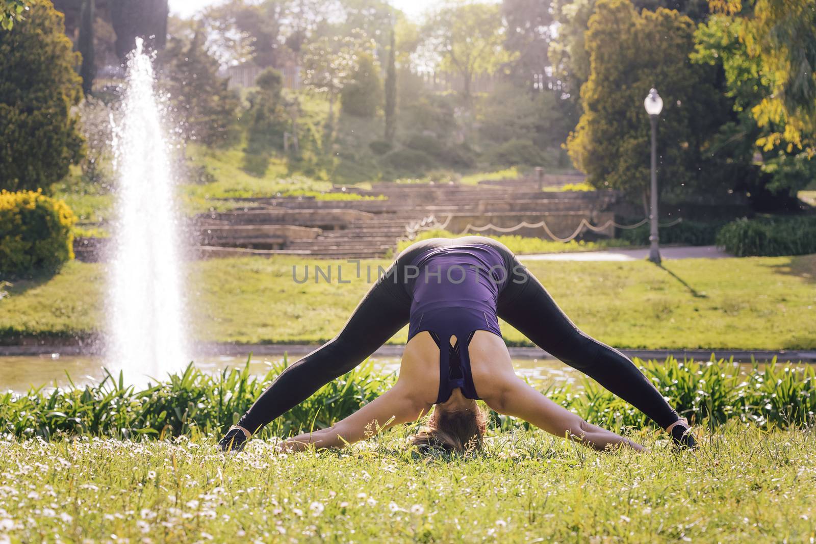 young sports woman training with flexibility exercises and stretching legs on the grass outdoors in the park, modern healthy lifestyle and sport concept, copy space for text