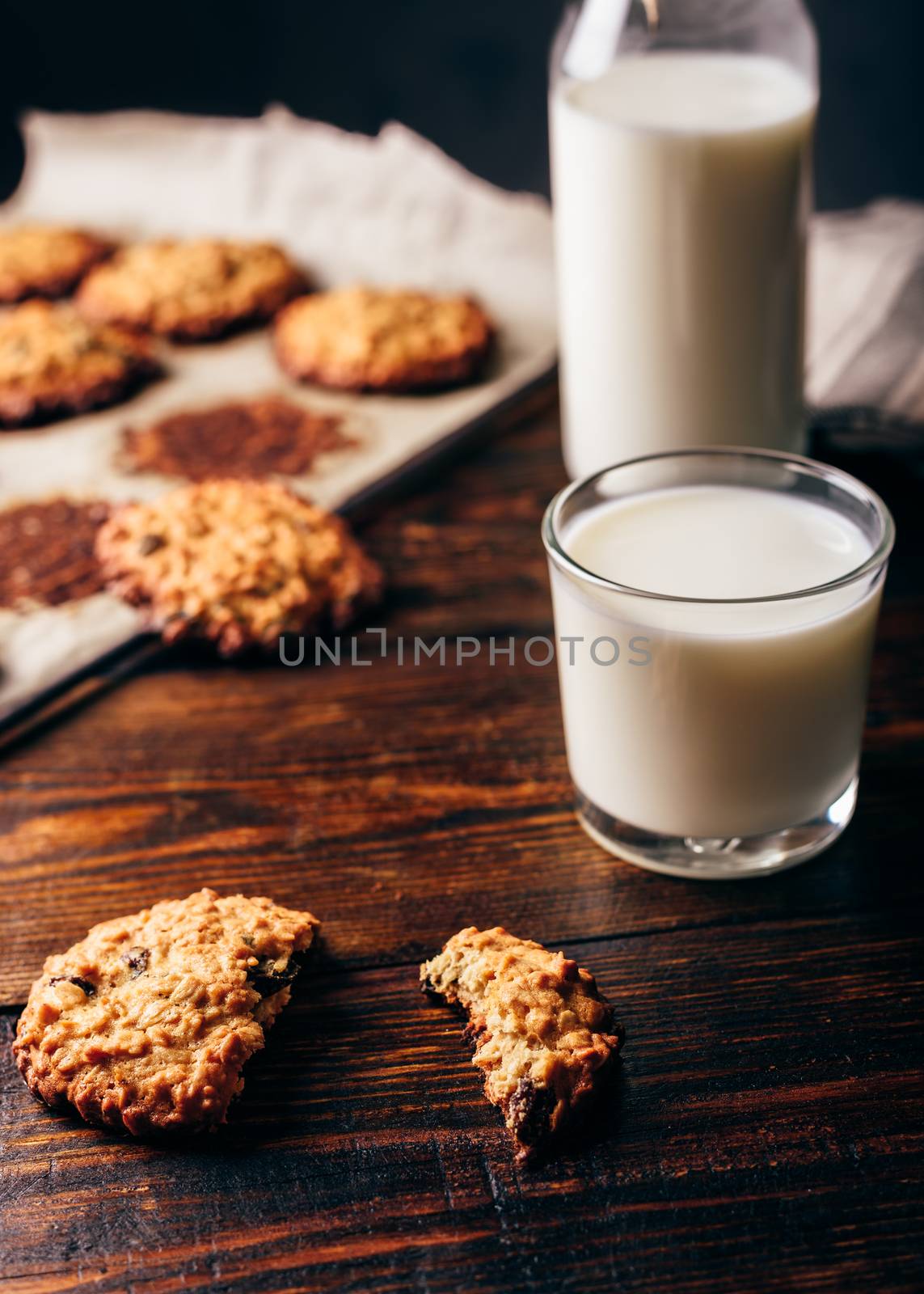 Oatmeal Cookies with Raisins and Glass of Milk for Breakfast. Some Cookies on Parchment Paper with Bottle on Backdrop. Vertical Orientation.