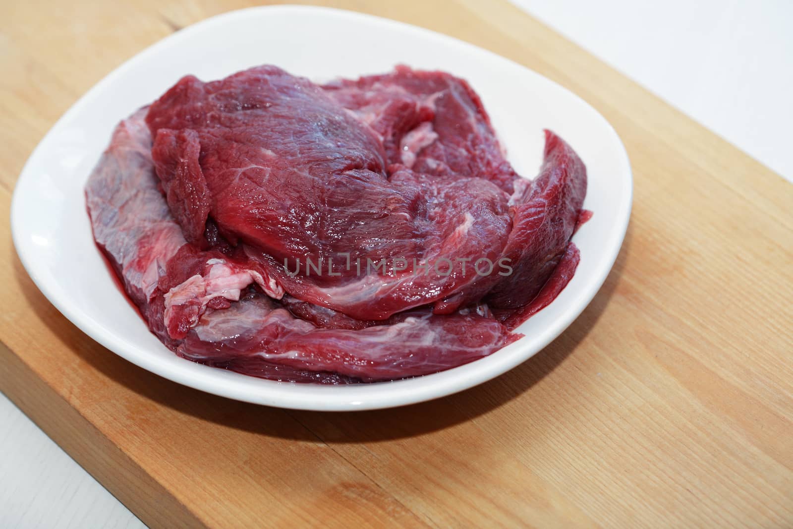 Portion of raw beef meat for cooking on white plate