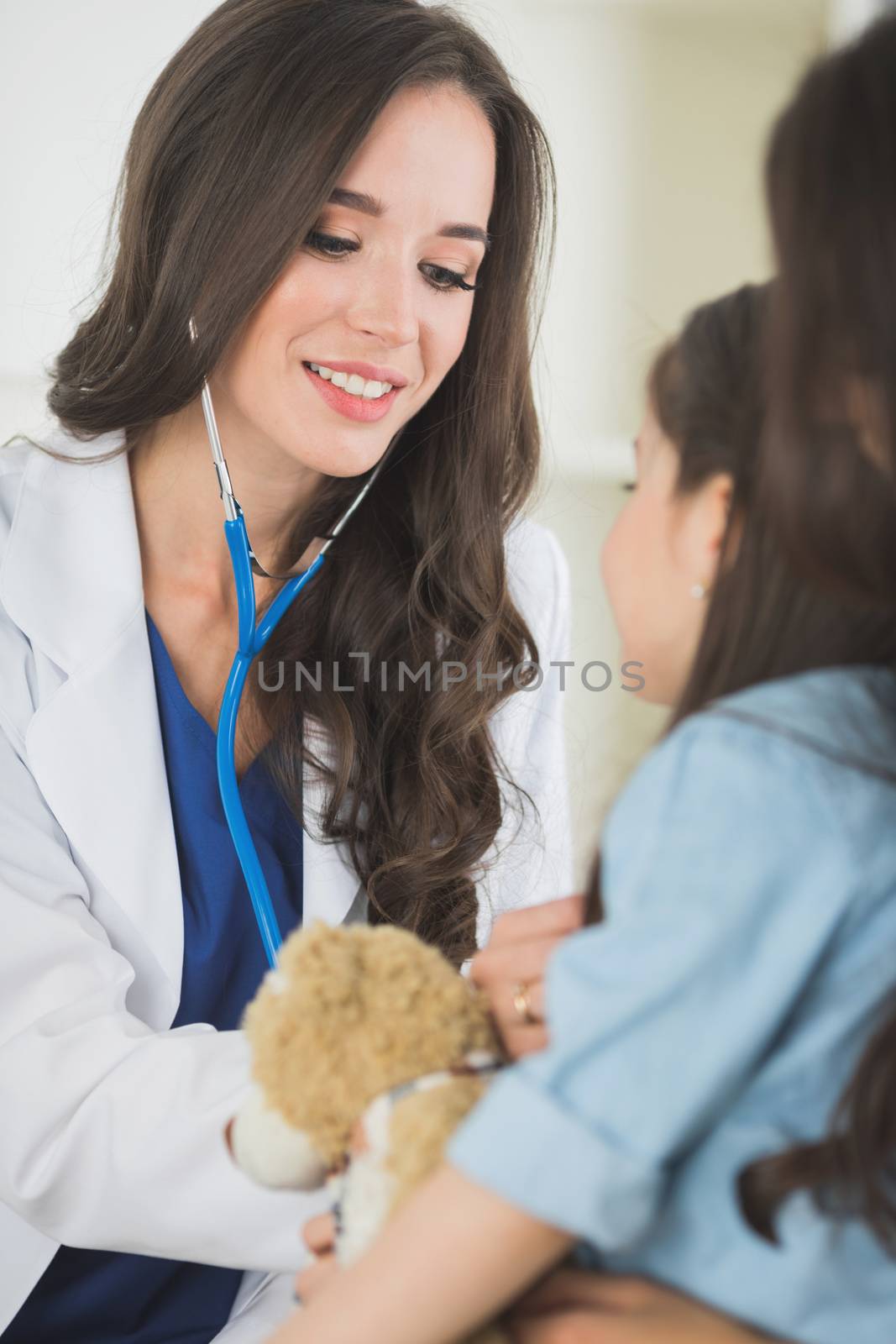 Female doctor and little girl with teddy bear sitting at the medical office.Child and doctor examining teddy bear