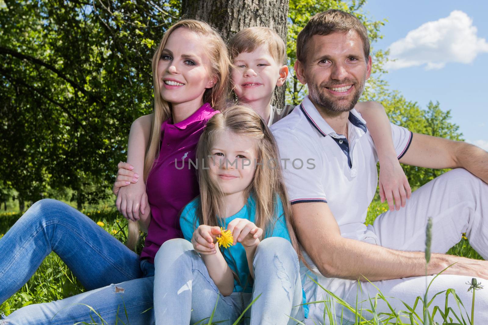 Father, mother and their children are sitting on the green grass in the summer park
