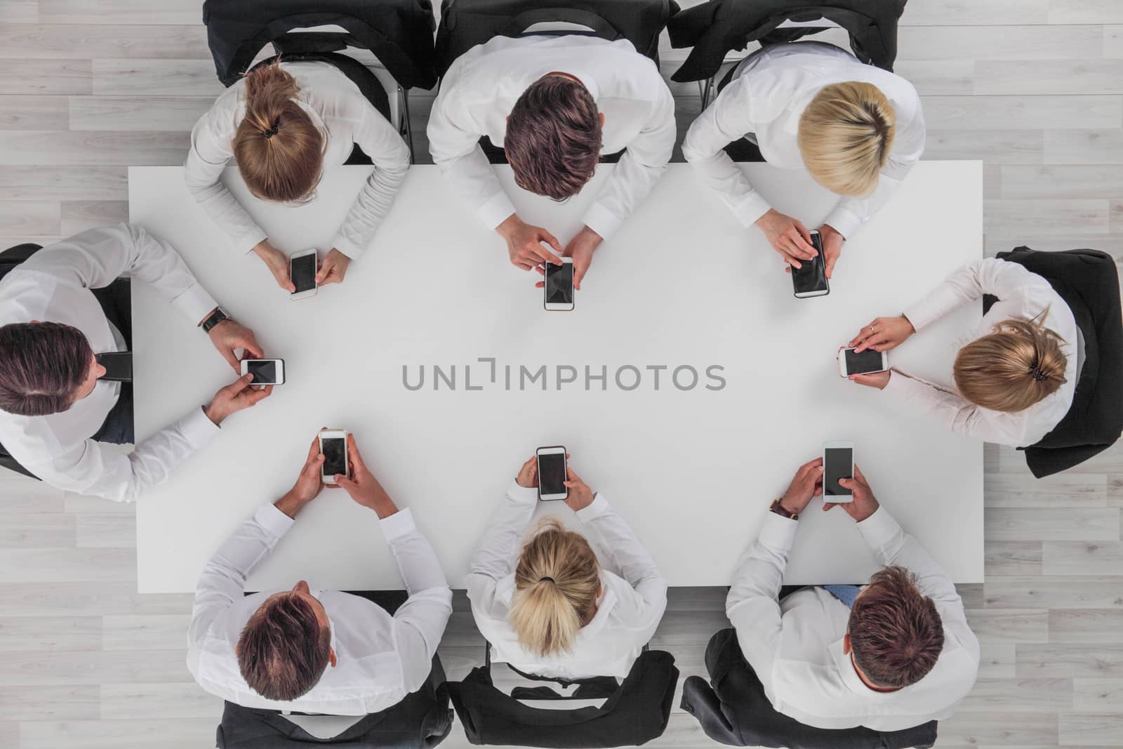 Top view of business people sitting around the table and using smartphones with blank screen