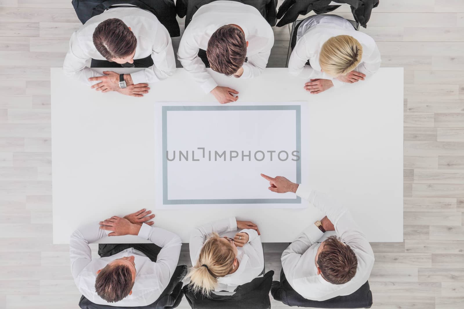 Business, people and team work concept - close up of creative team sitting at table and pointing finger to blank copy space for text