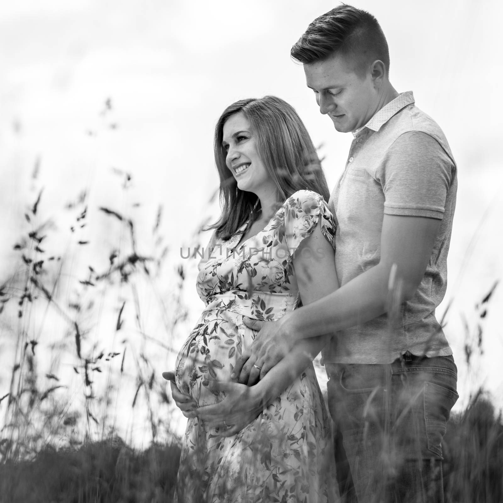 Young happy pregnant couple hugging in nature. Concept of love, relationship, care, marriage, family creation, pregnancy and parenting. Artistic black and white image.