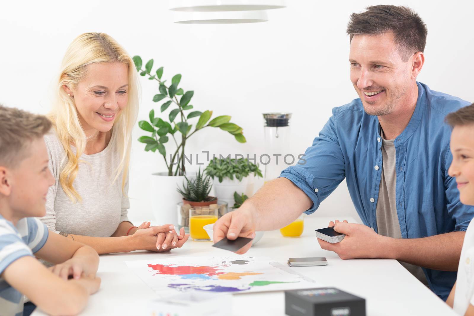 Happy young family playing card game at dining table at bright modern home. by kasto