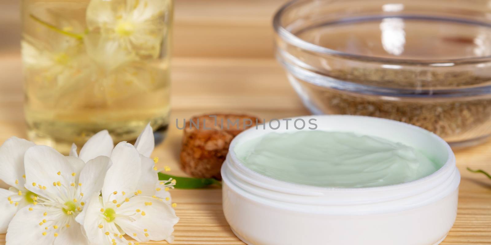 Jar of cream made from natural plant ingredients, oils and herbs, jasmine flowers on a light wooden background - preparation of organic cosmetics concept, close up.