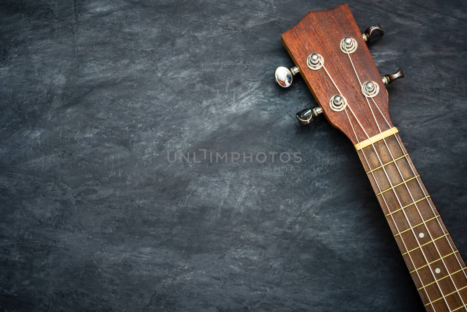 Ukulele on black cement background. Headstock and fret of ukulele parts. Copy space for text. Concept of Hawaiian musical instruments and music lovers.