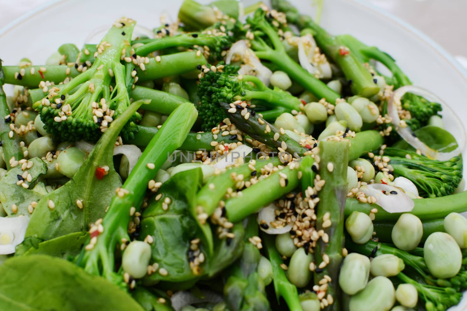 Tasty spring salad of baby broccoli, asparagus, broad beans, spinach leaves and shallot dressed with sesame and nigella seeds