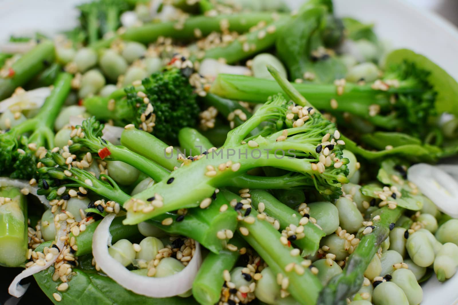 Broccolini, French beans and broad beans in a fresh salad, dressed with oil and sesame and nigella seeds  