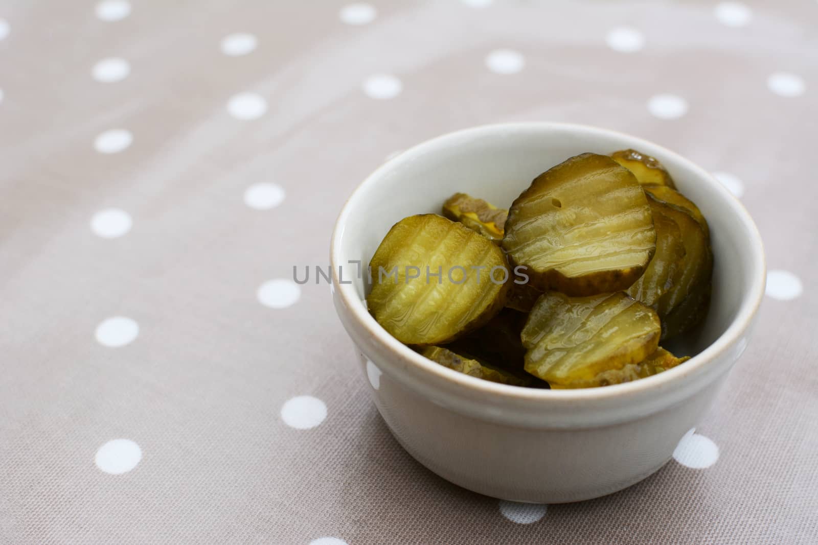 Slices of juicy, sour gherkins in a small ceramic pot on a dining table with copy space