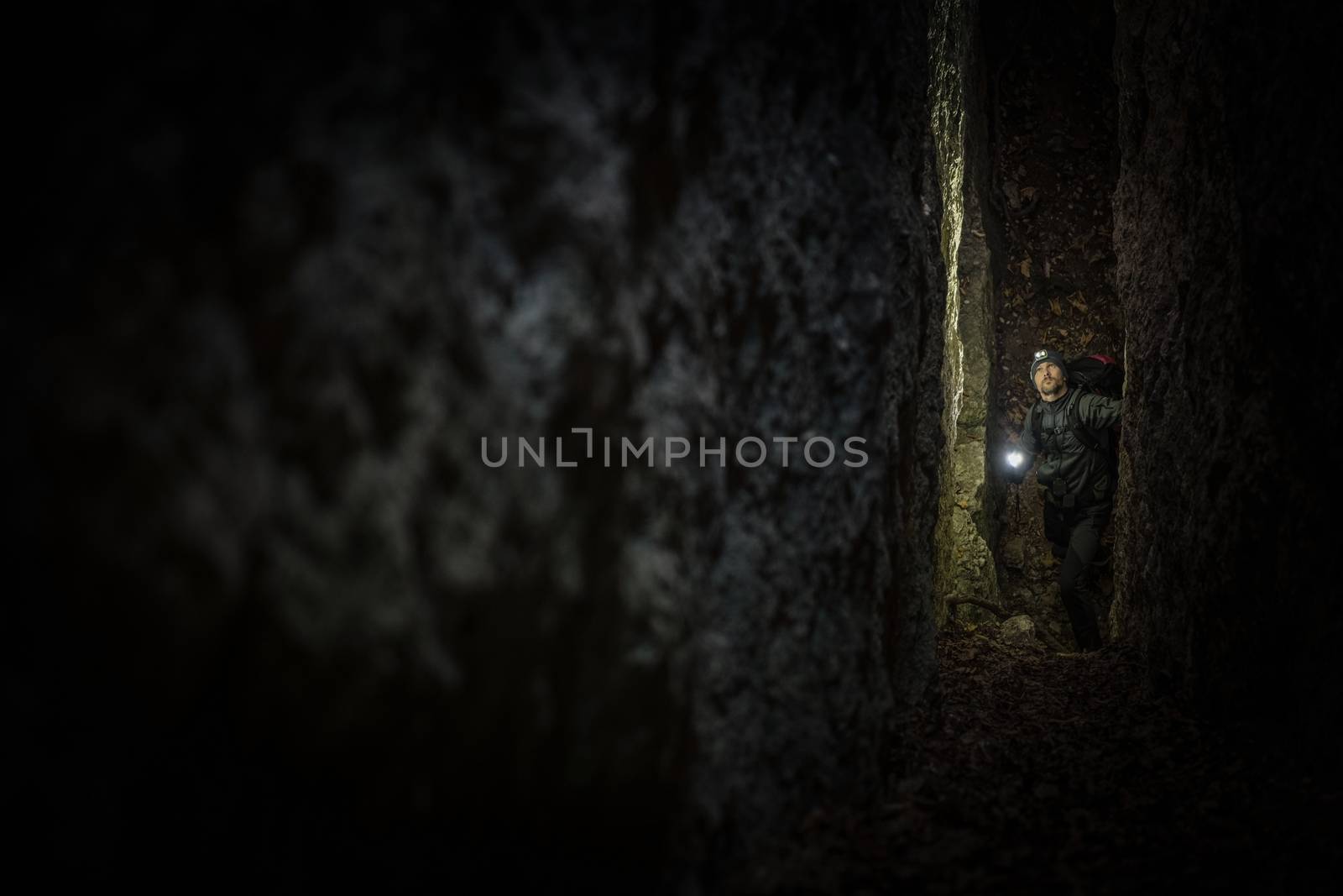 Narrow Cave Expedition. Caucasian Men in His 30s with Flashlight Exploring Rock Formations. Extreme Activities.