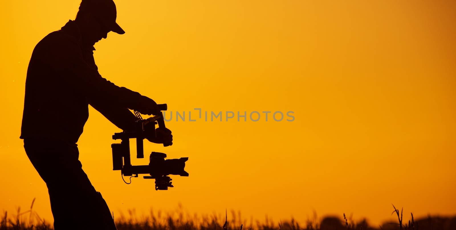 Video Stabilizer Operator. Taking Video Shoots Using DSLR Gimbal Equipment. Sunset Silhouette Concept.