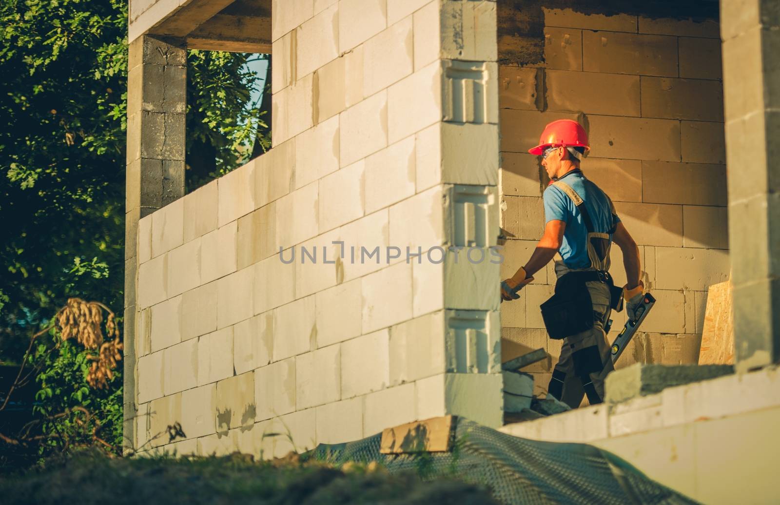 Caucasian House Construction Worker in Hard Hat Going with Spirit Level To Check Necessary House Levels.