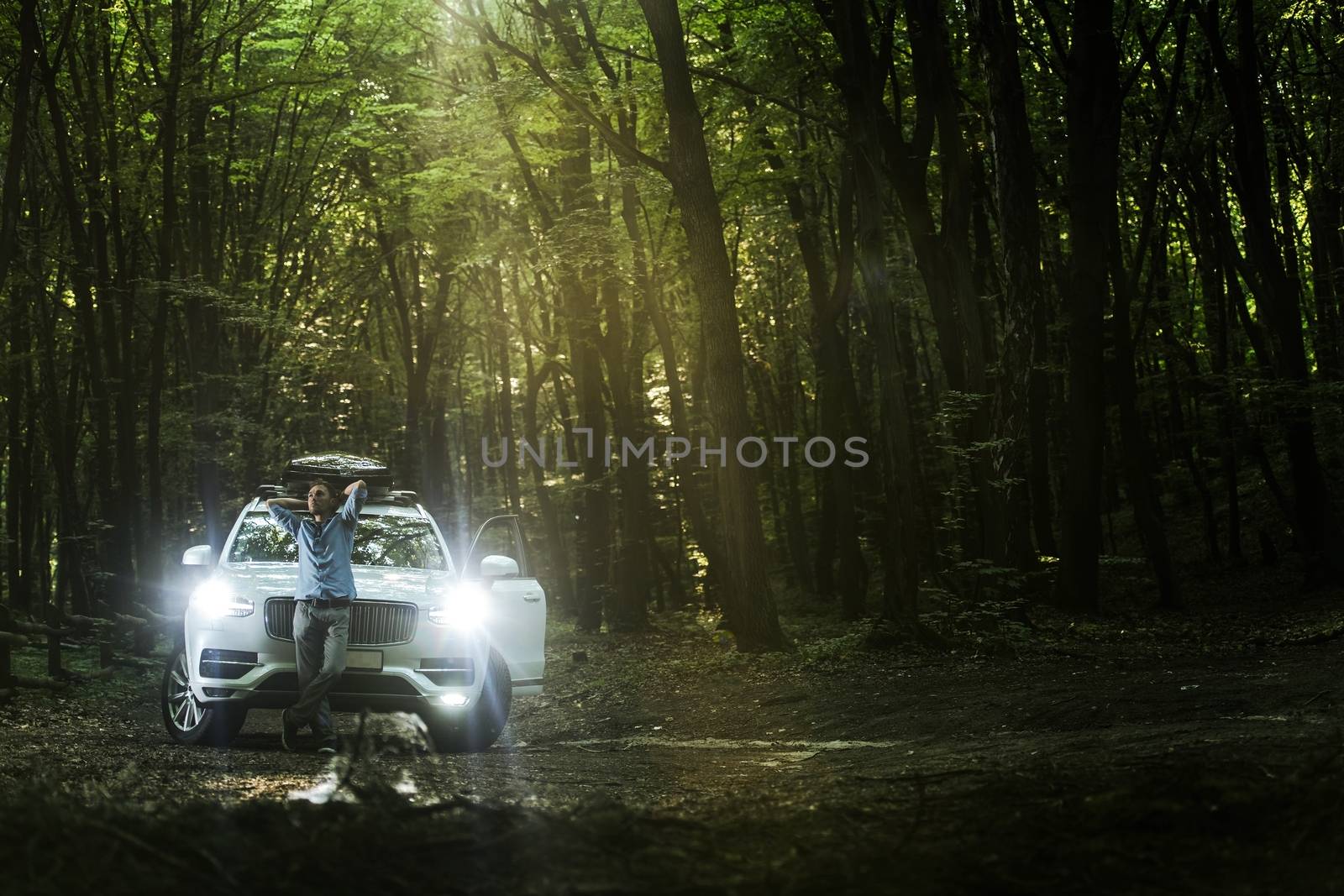 Quick Getaway From the Noises of the City. Young Caucasian Businessman Looking For Calm and Peace in the Local Forest Preserve. Men Relaxing in the Forest with Hand Behind Head in Front of His Company Car.