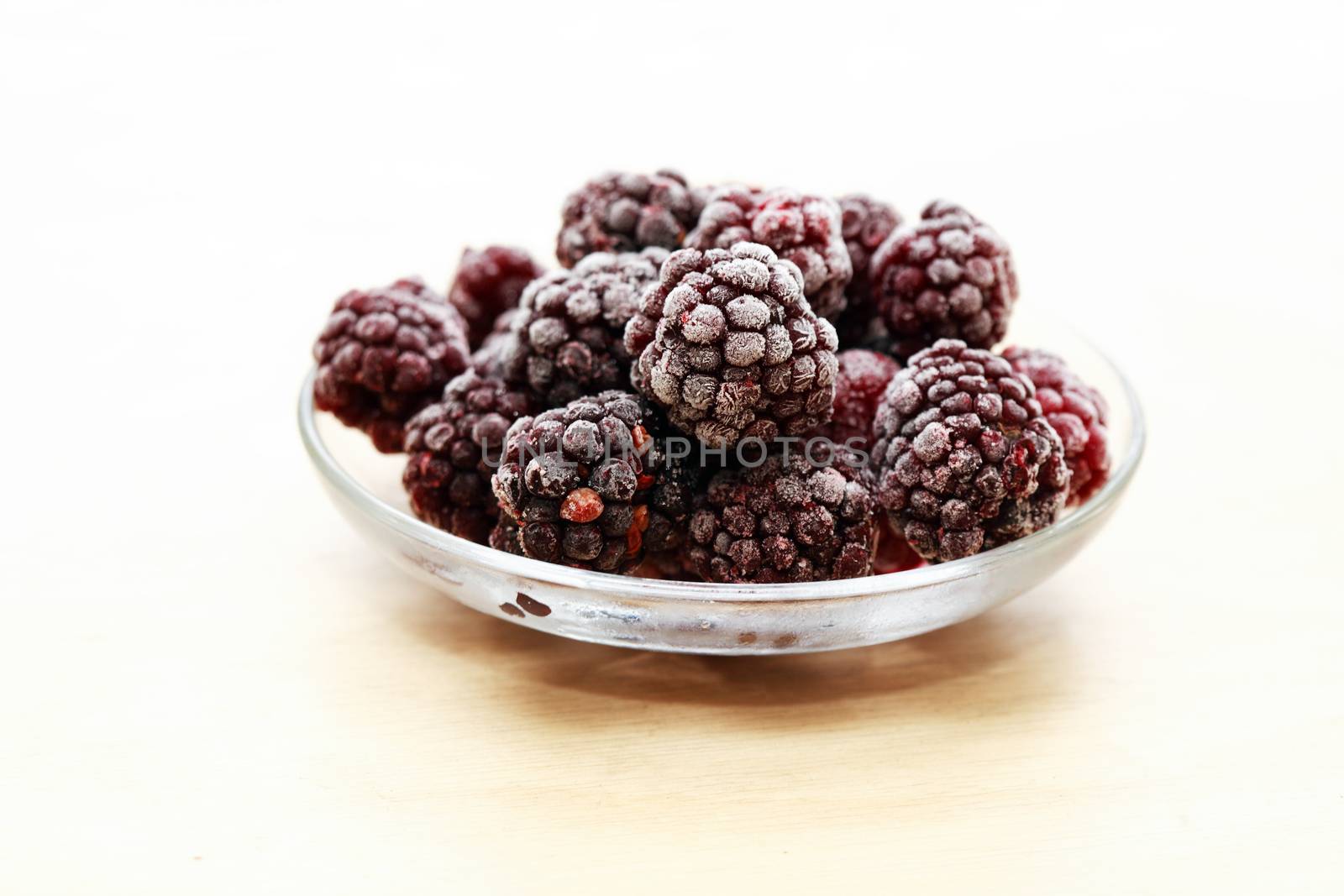 Saucer with heap of frozen blackberry fruits on wood