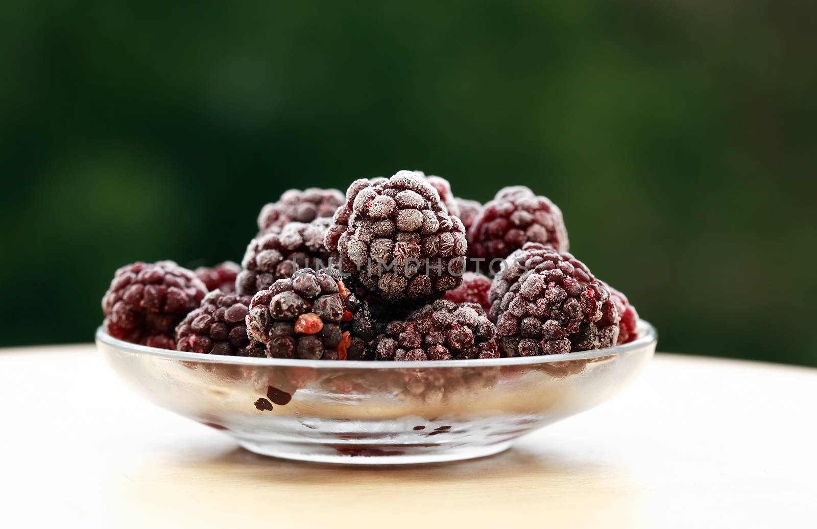 Saucer with heap of frozen blackberry fruits on wood