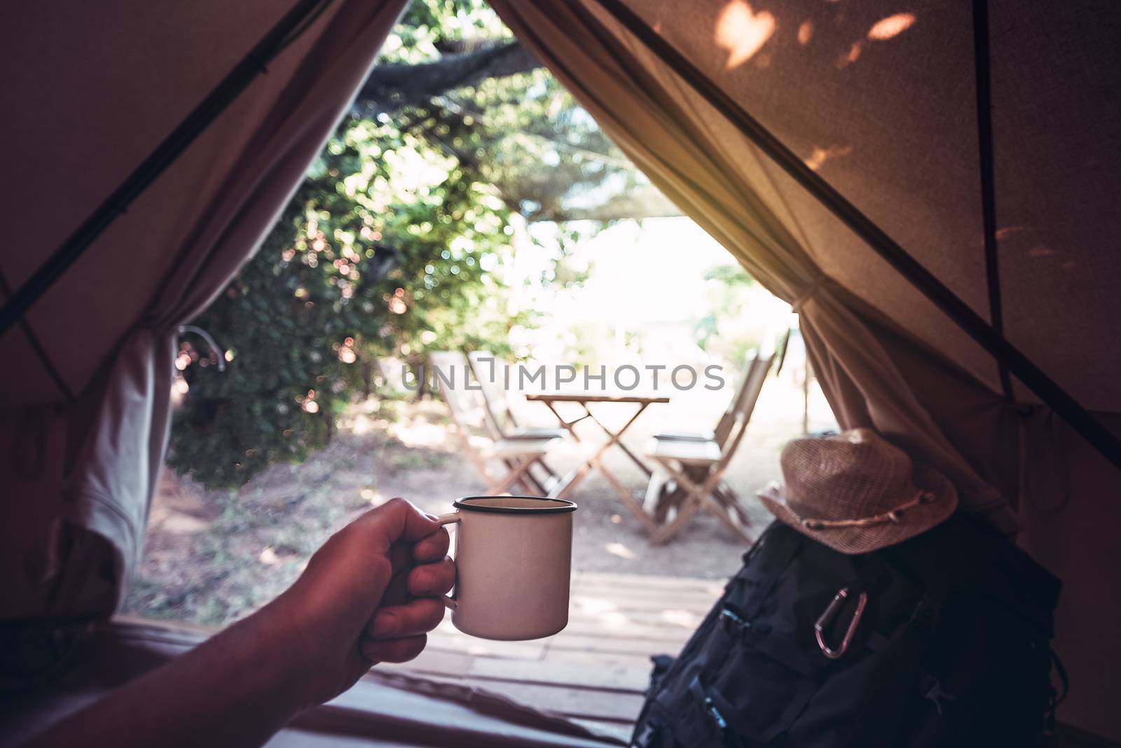 view of a hand of a hiker person resting with a cup in a camping tent, travel discovery concept, point of view shot