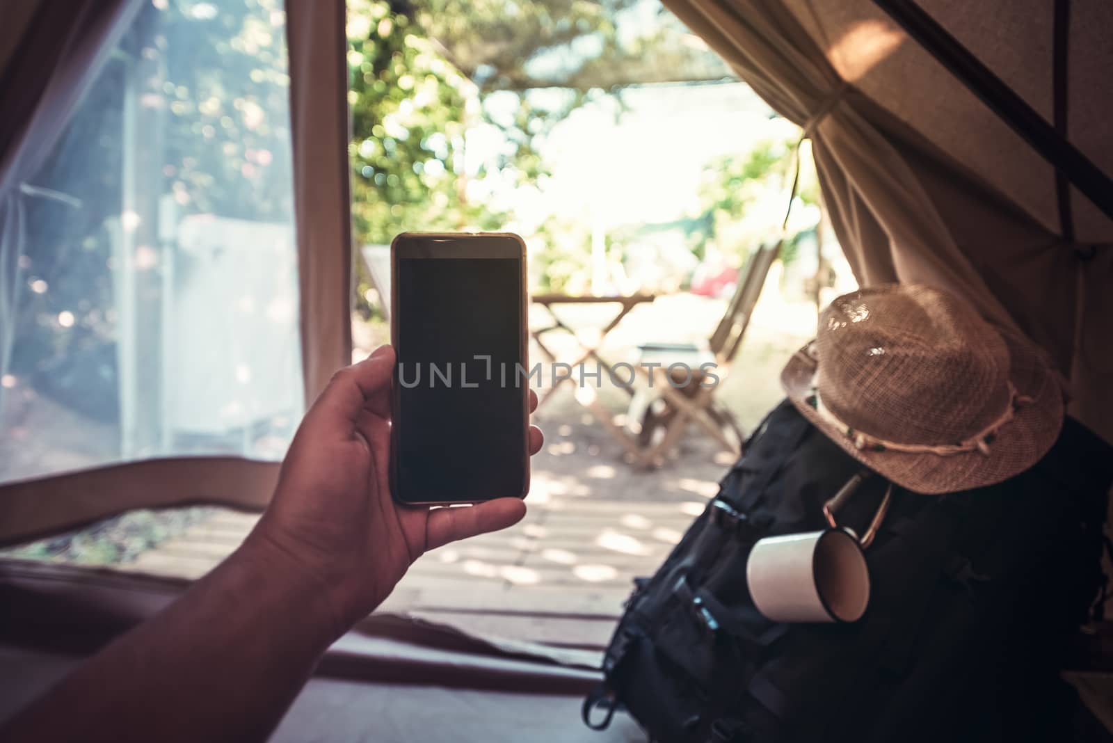 view of a hand of a hiker man resting while consulting the phone in a camping tent, travel discovery concept, point of view shot