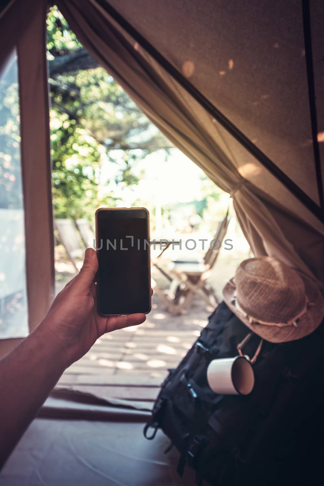 vertical view of a hand of a hiker person resting while consulting the phone in a camping tent, travel discovery concept, point of view shot