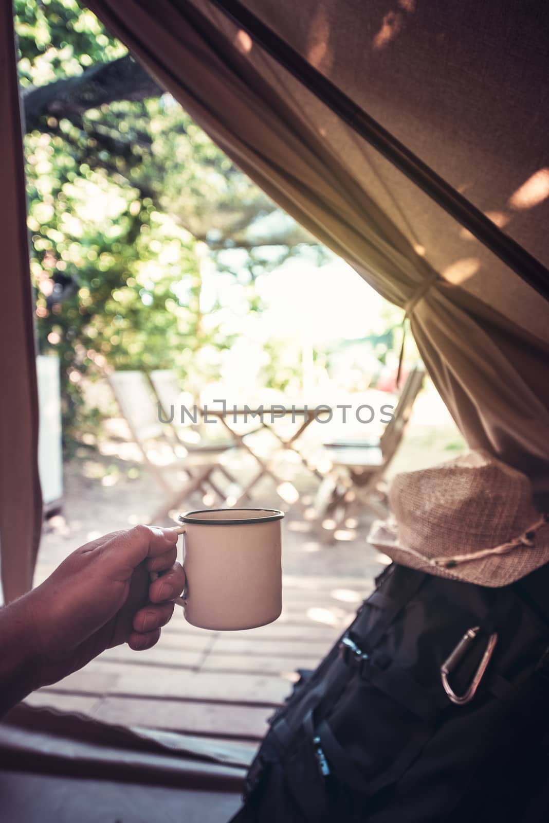 vertical view of a hand of a hiker man resting with a cup in a camping tent, travel discovery concept, point of view shot