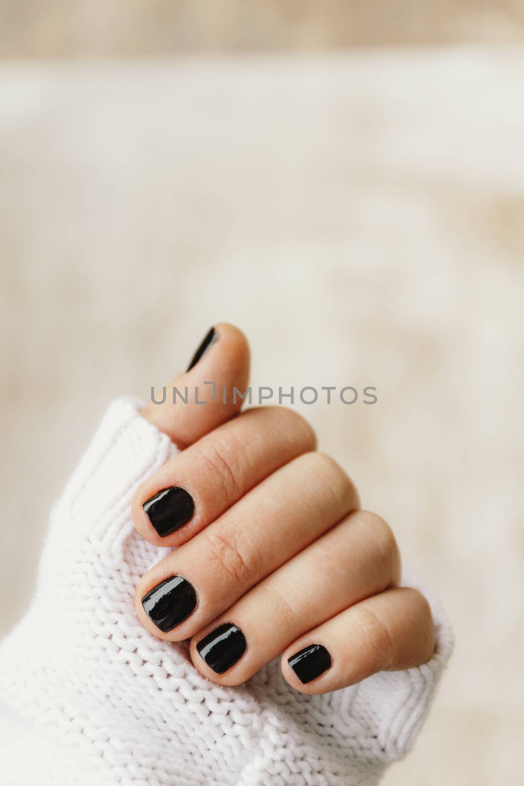 hand with black manicure on short nails in a white sweater on a light background. The concept of a stylish and warm winter.