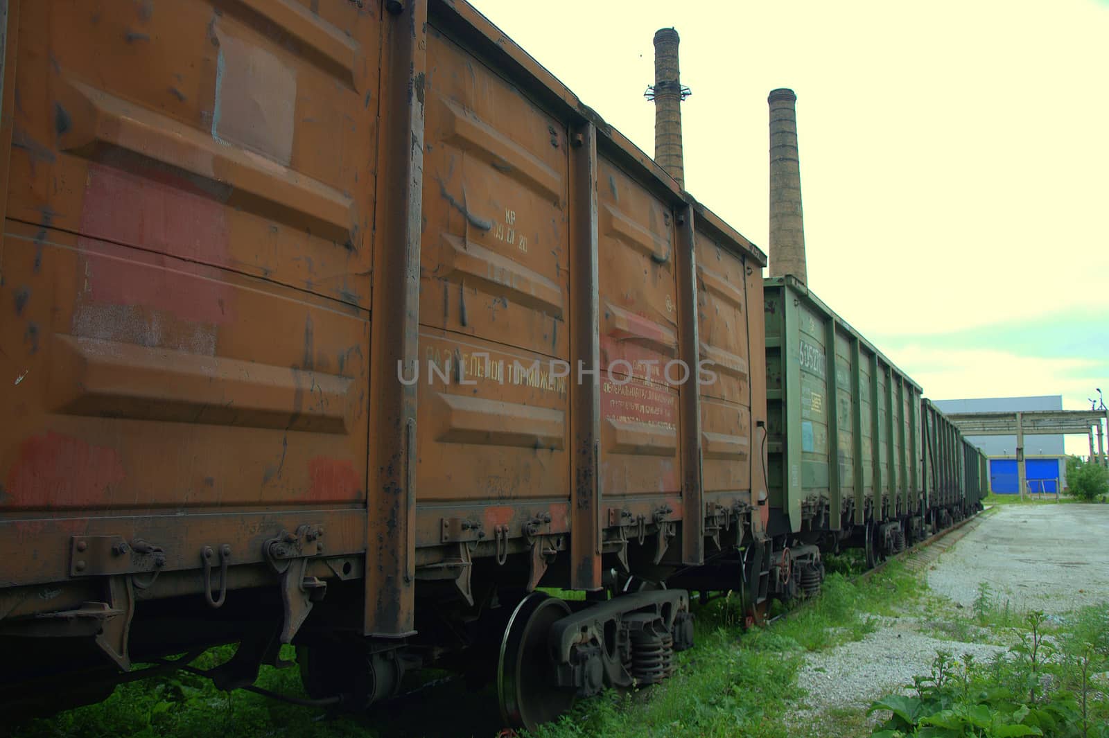 Railway cars are at an impasse in front of the old plant on the background of pipes.