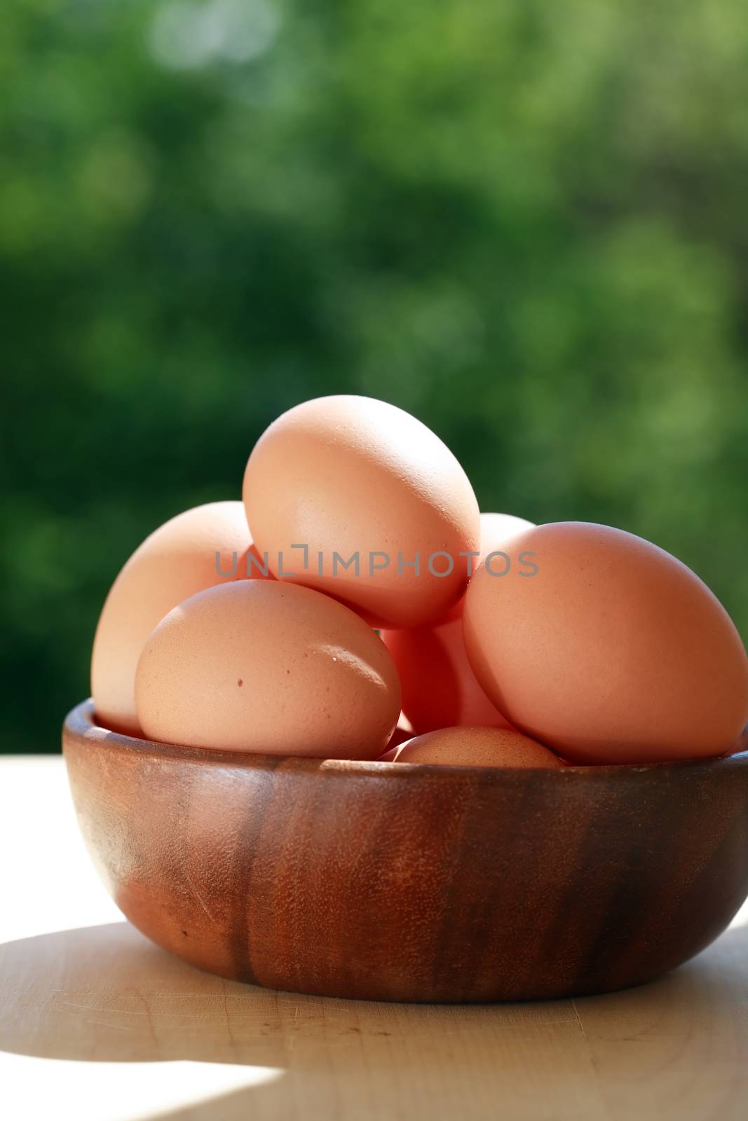 Heap of chicken eggs in wooden bowl against green nature background
