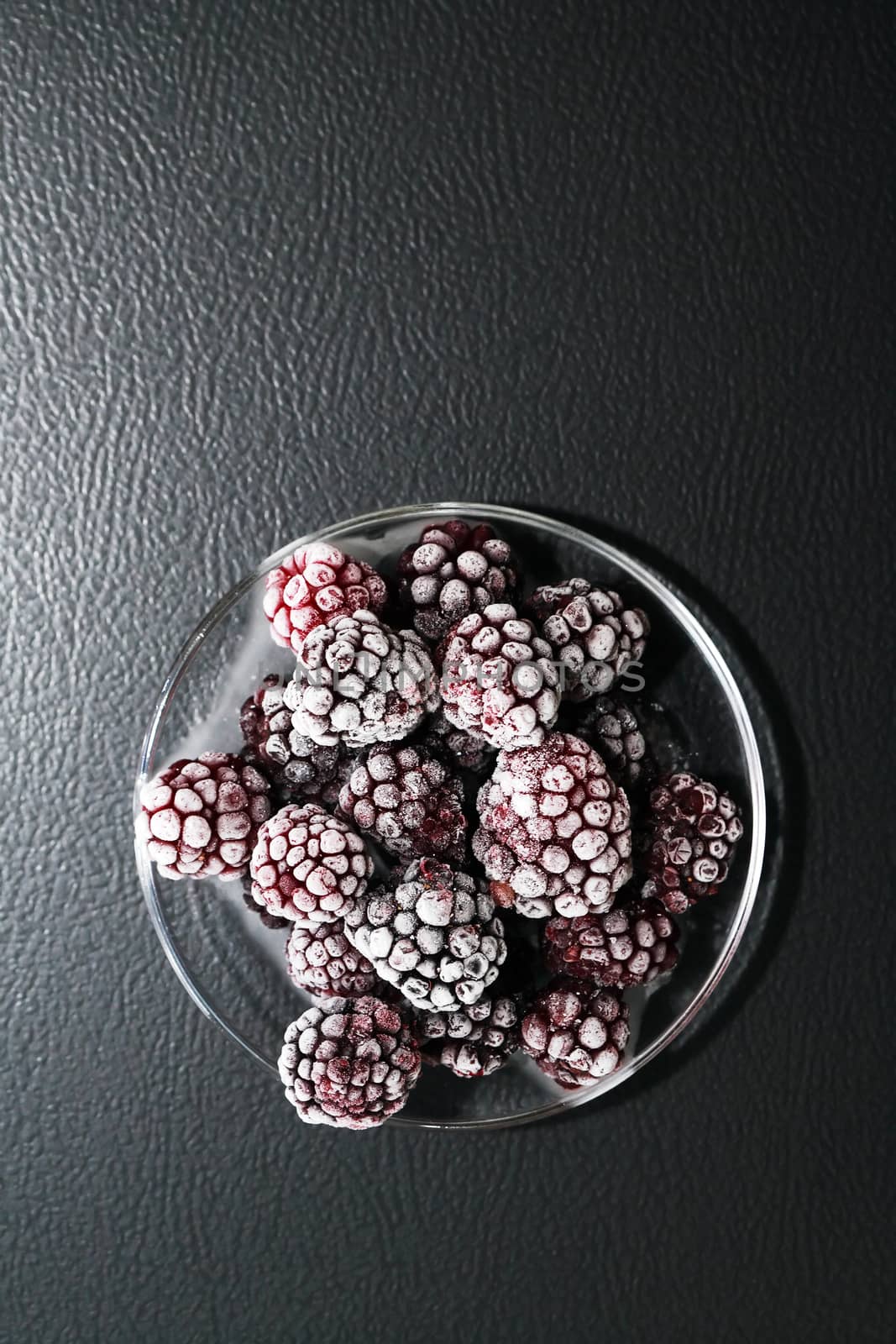 Saucer with heap of frozen black berry fruits on dark background