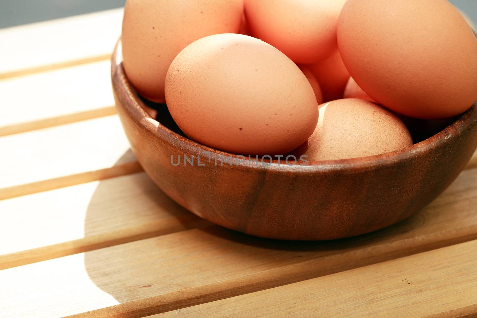 Heap of chicken eggs in wooden bowl on timber background