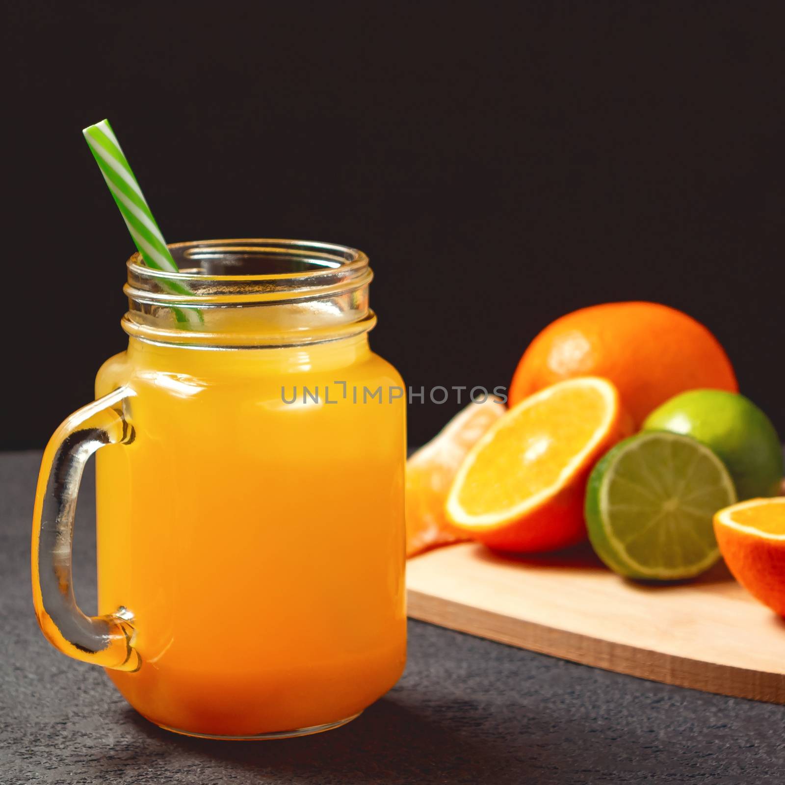 Freshly made citrus juice from oranges, grapefruit and lime in a jar-mug with a straw on black table.