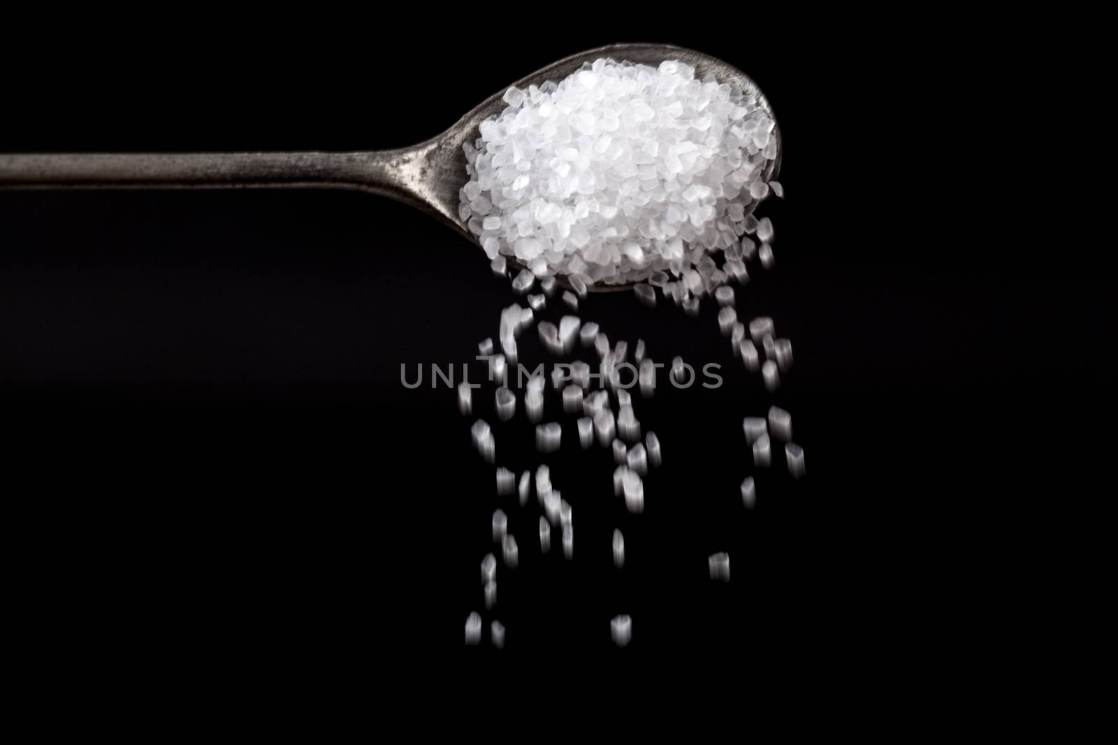 White Sea Salt Crystals Pouring From Silver Spoon on Black Background