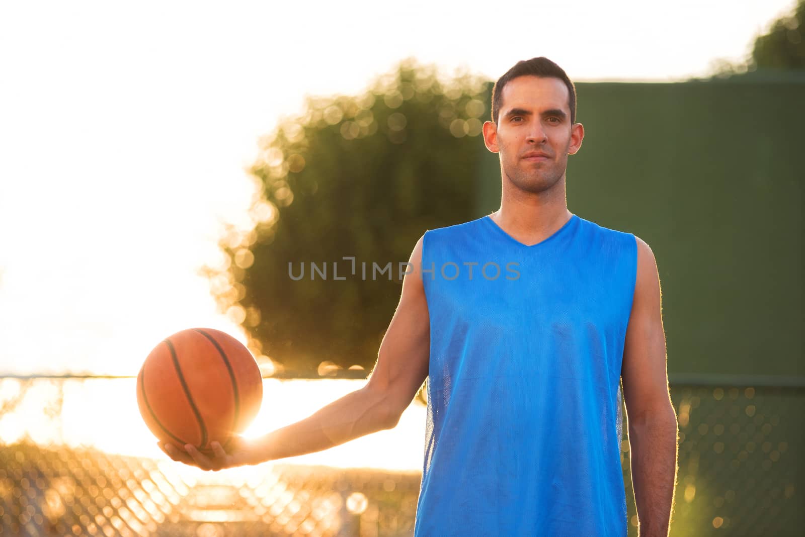 Athlete man holding basketball ball standing on playground at sunset