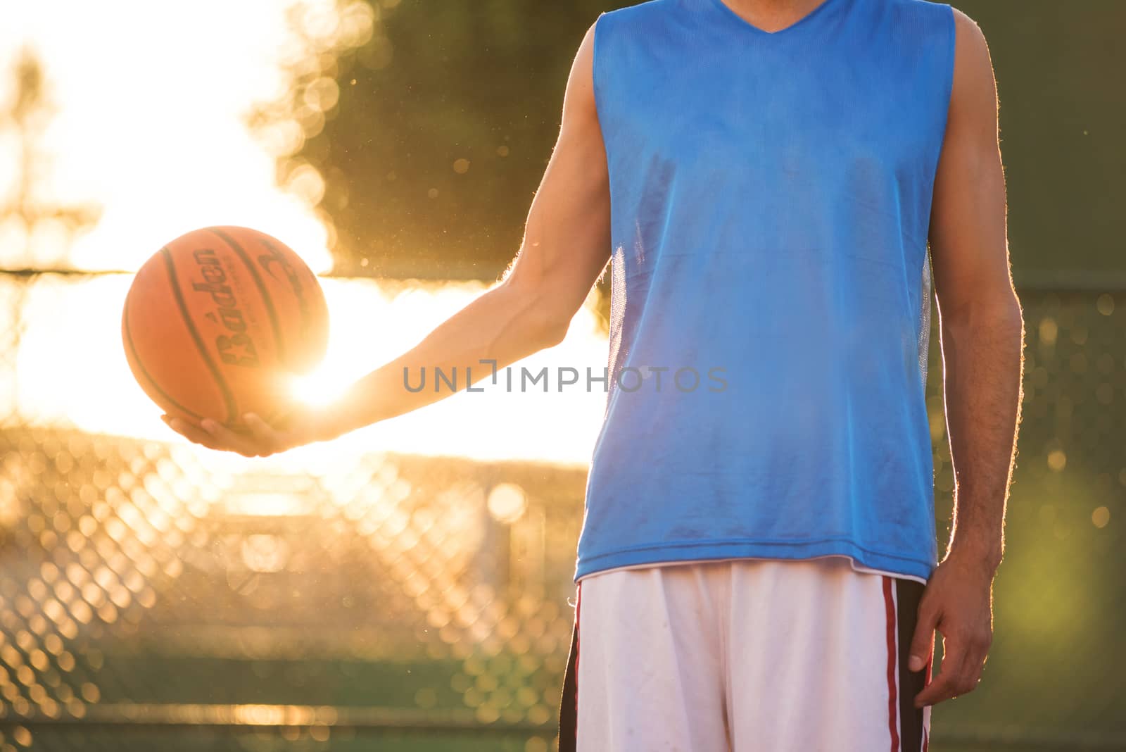 Athlete man holding basketball ball standing on playground at sunset