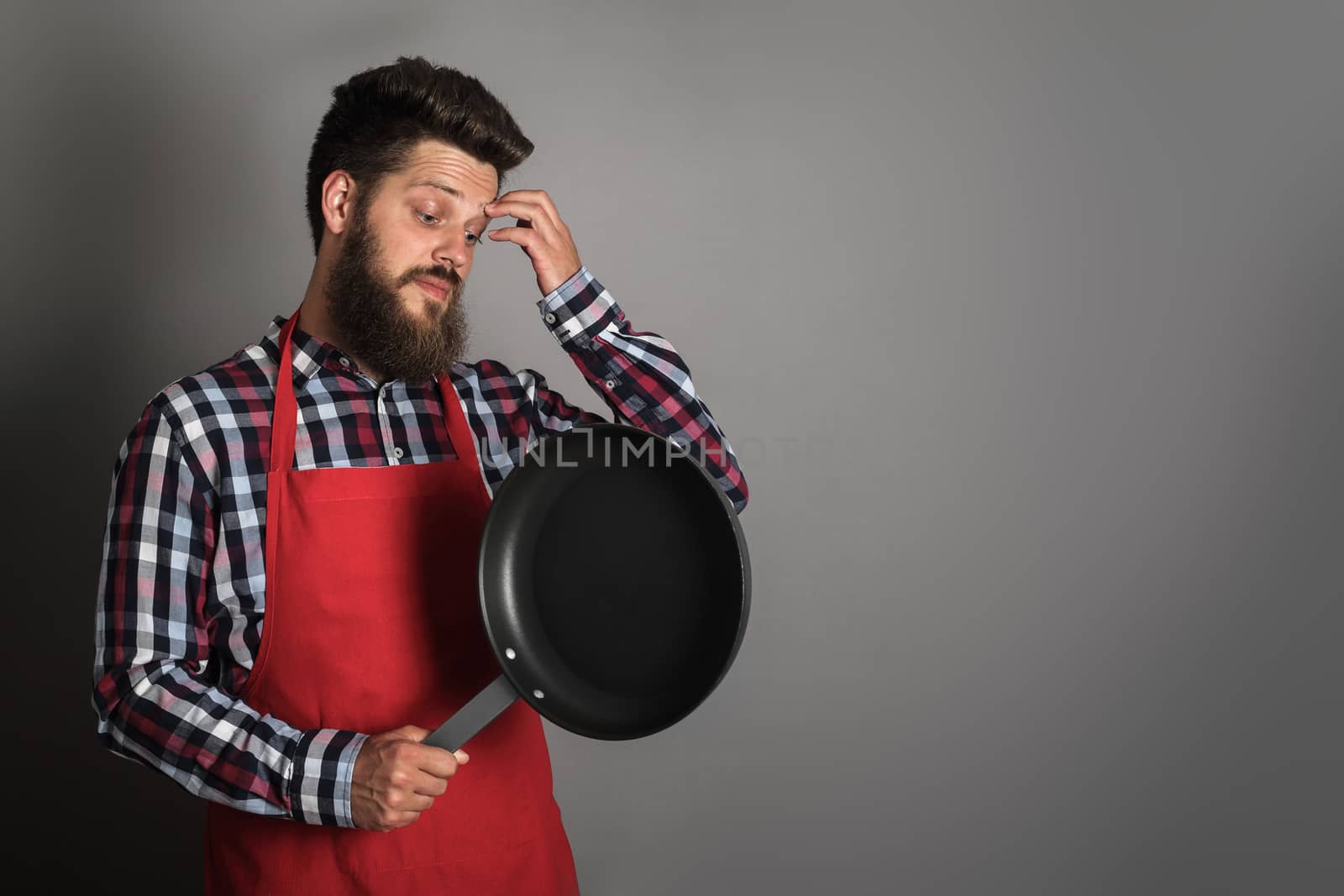 Man in red apron looking at frying pan and thinking what to do