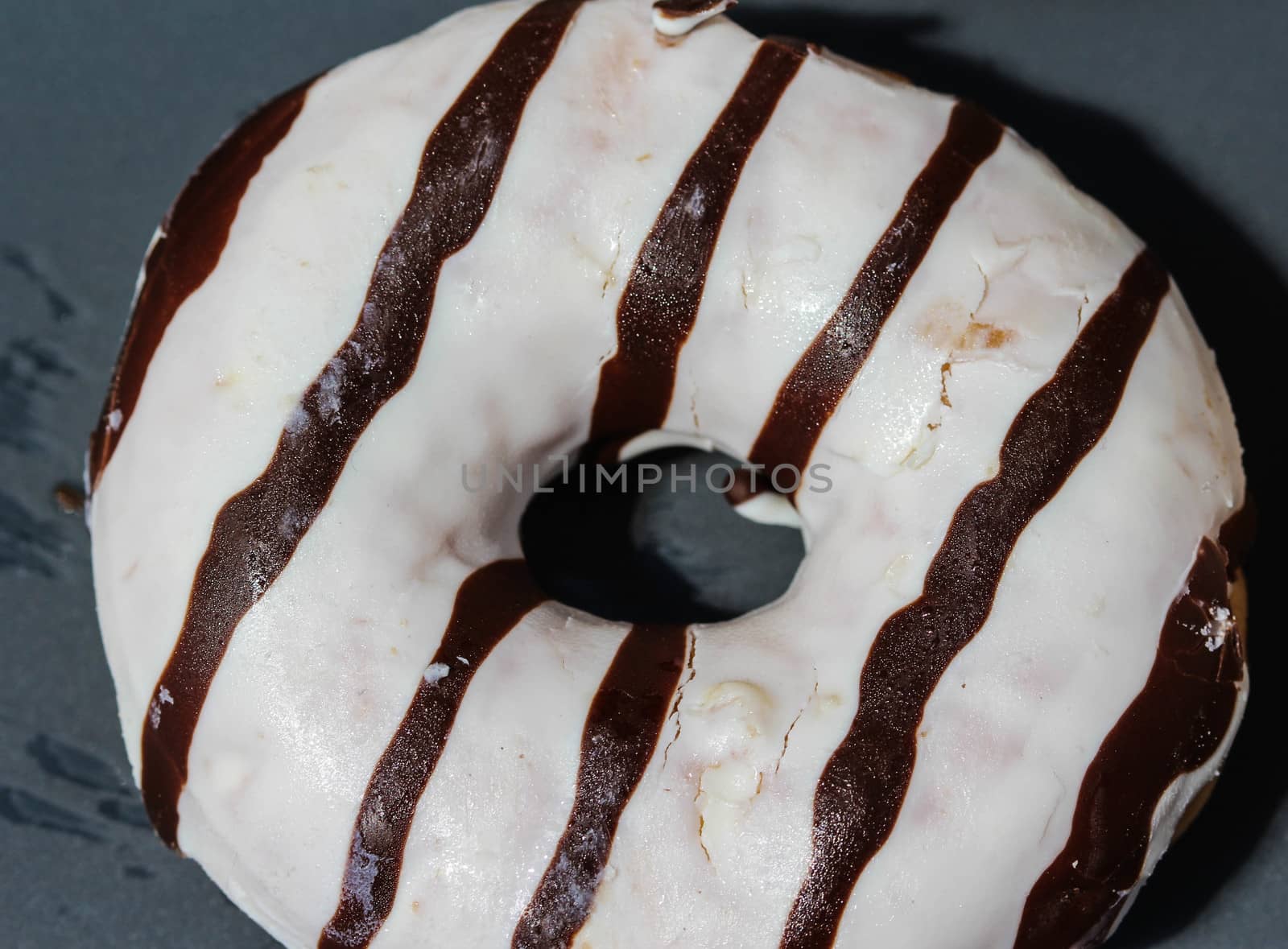 close up of vanilla donuts on table. The donuts have white glaze with brown chocolate