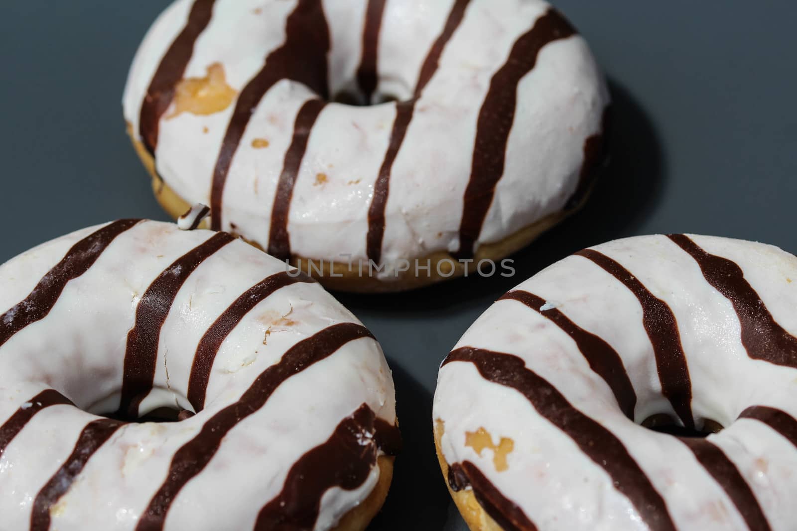close up of vanilla donuts on table. The donuts have white glaze with brown chocolate