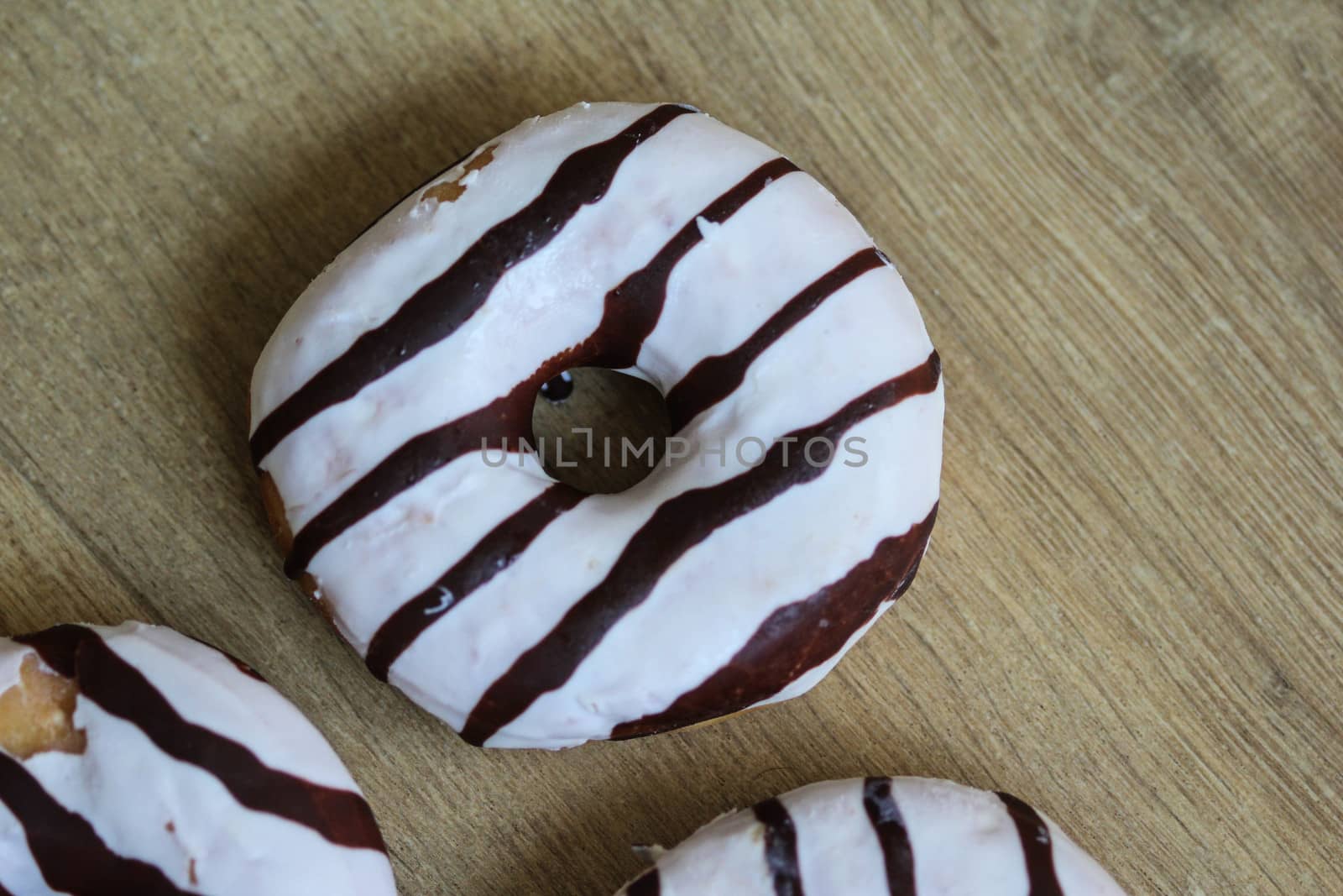 close up of vanilla donuts on table. The donuts have white glaze with brown chocolate