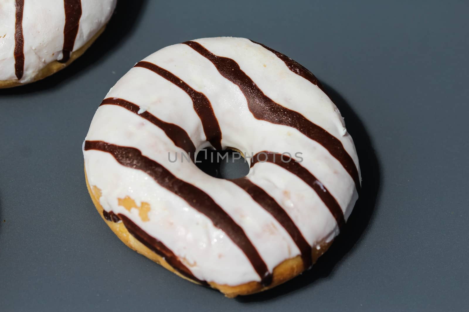 close up of vanilla donuts on table. The donuts have white glaze with brown chocolate