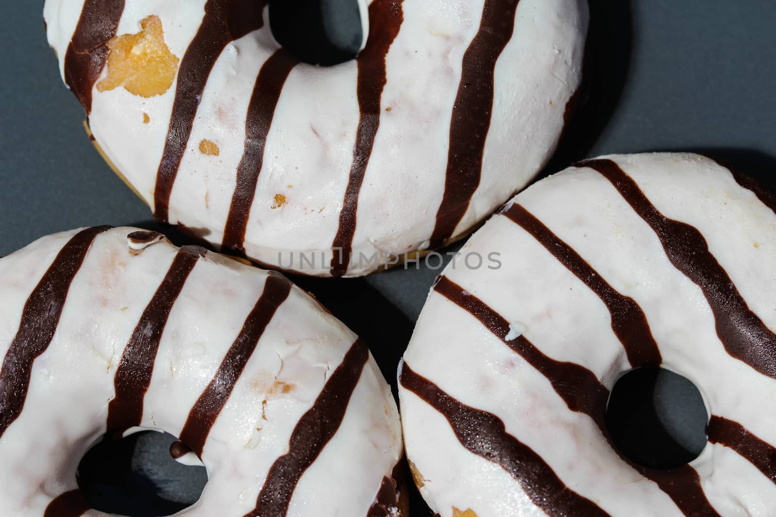 close up of vanilla donuts on table. The donuts have white glaze with brown chocolate