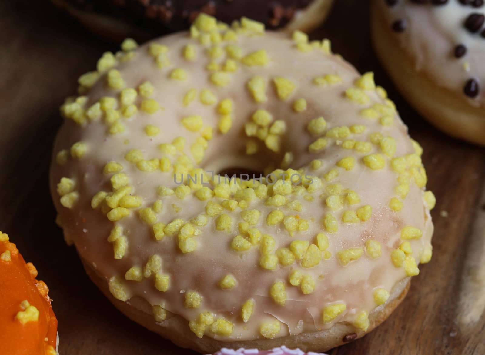 close up of a single strawberry donut with sprinkles on a wooden background