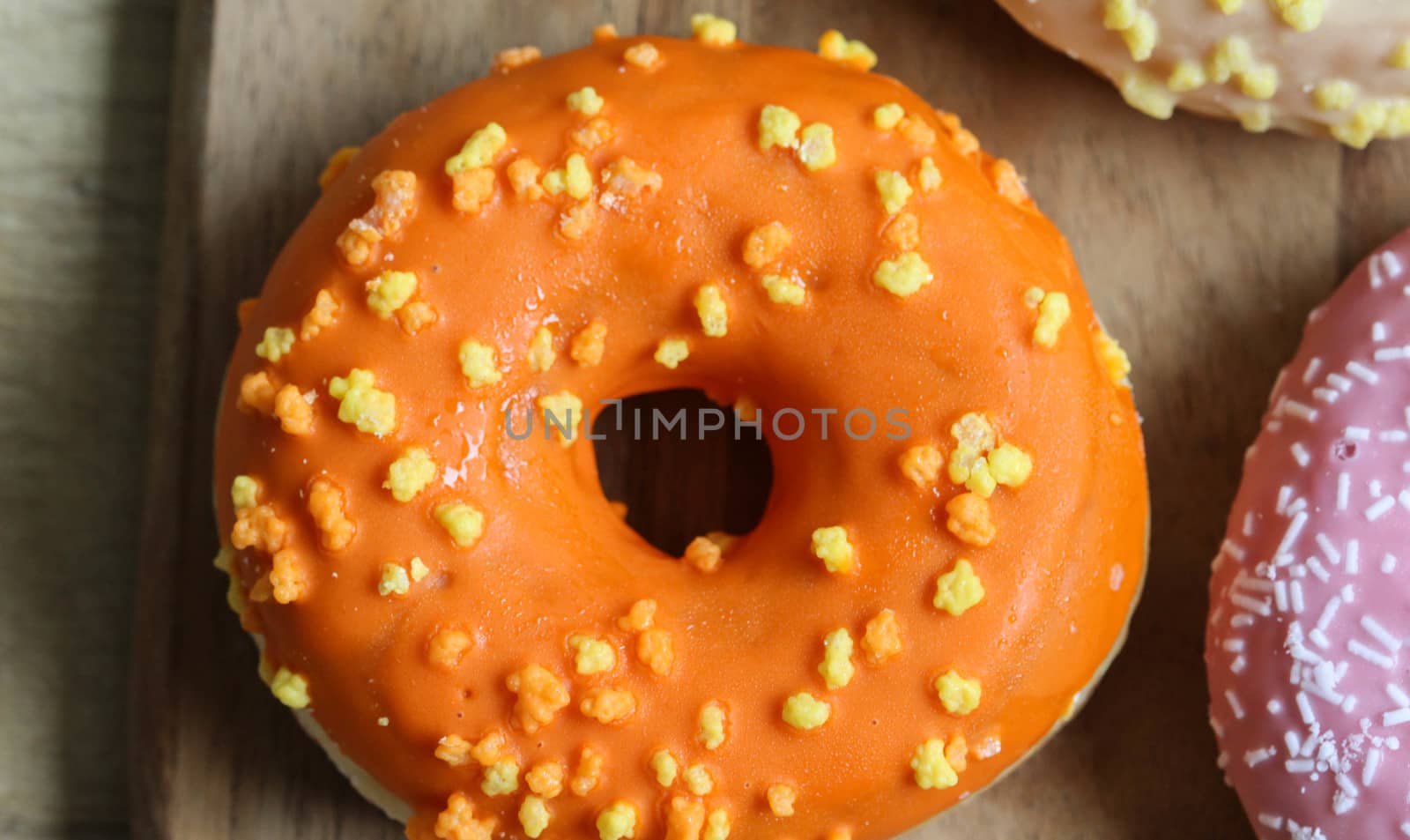 close up of a single orange donut with sprinkles on a wooden background
