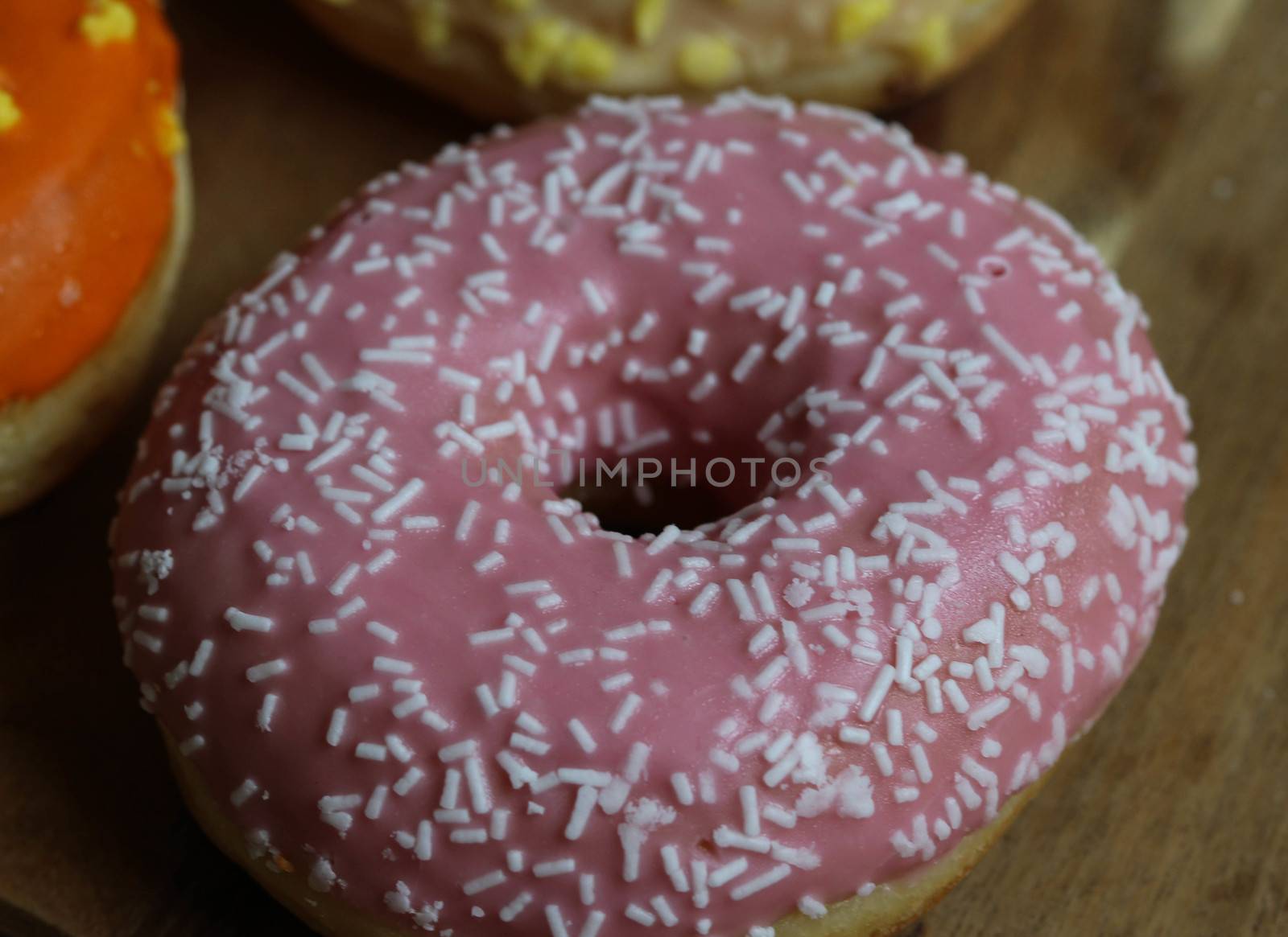 close up of a single strawberry donut with sprinkles on a wooden background