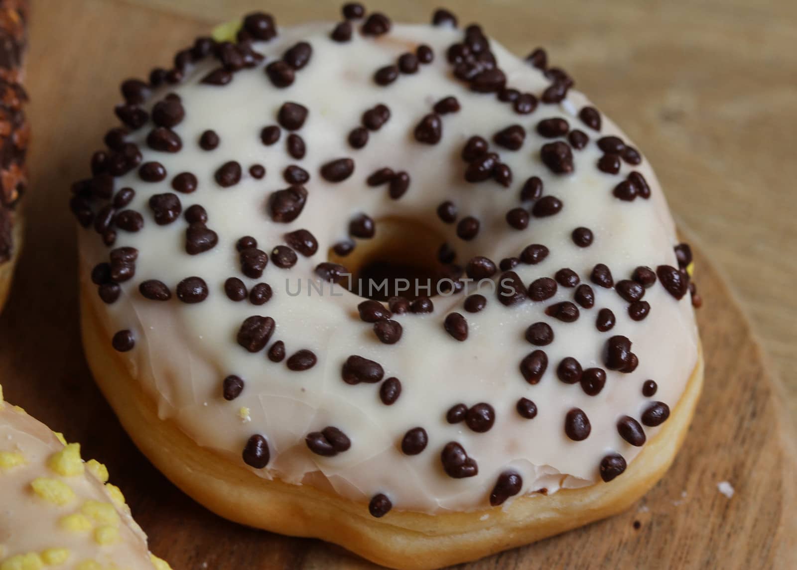 close up of vanilla donuts on table. The donuts have white glaze with brown chocolate