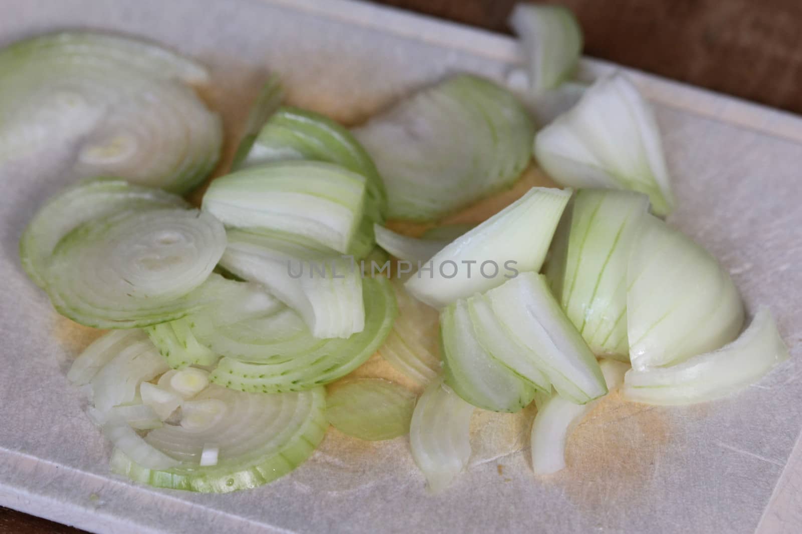 fresh healthy cutted onion on white cutting board on wooden background by michaelmeijer