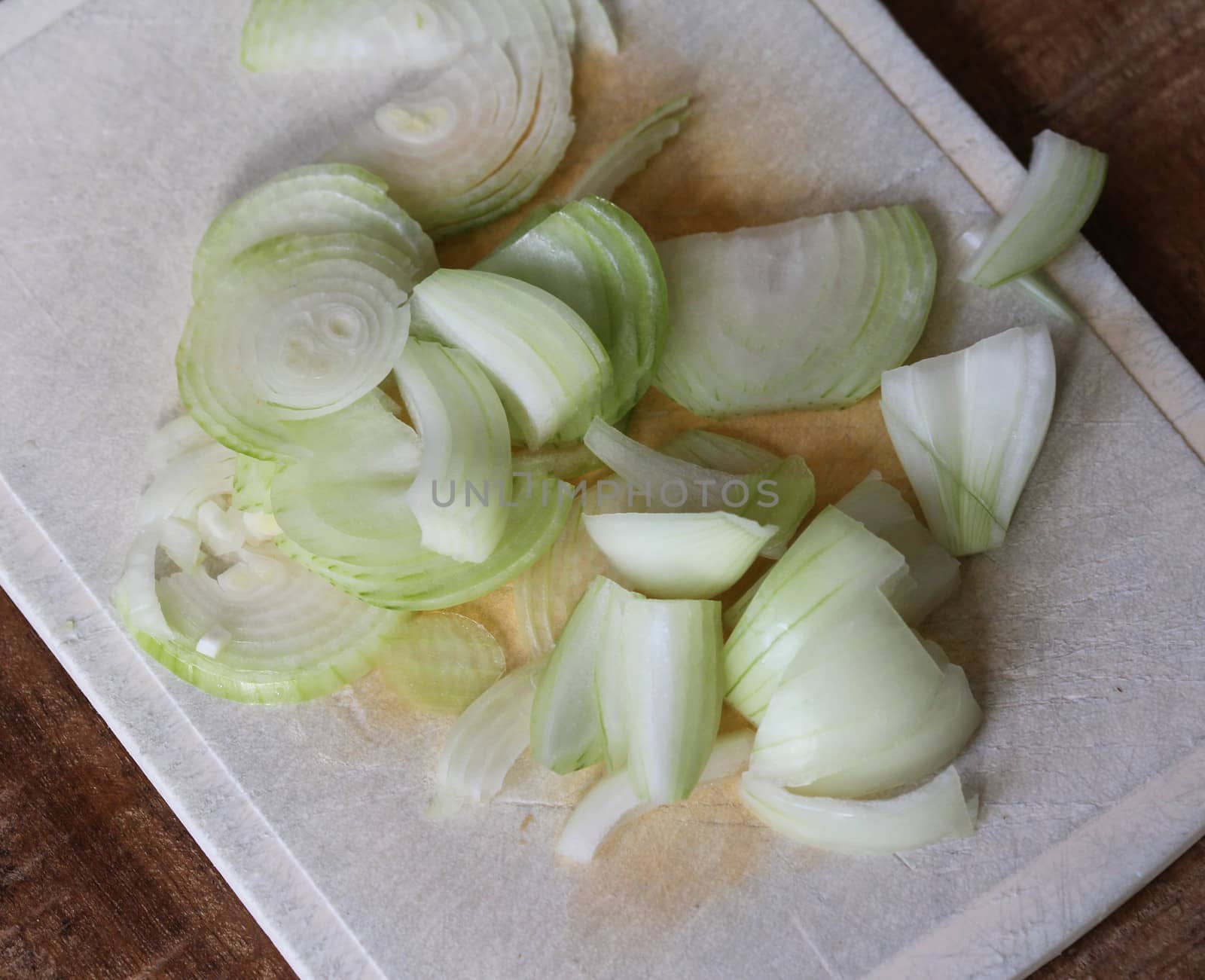 fresh healthy cutted onion on white cutting board on wooden background by michaelmeijer