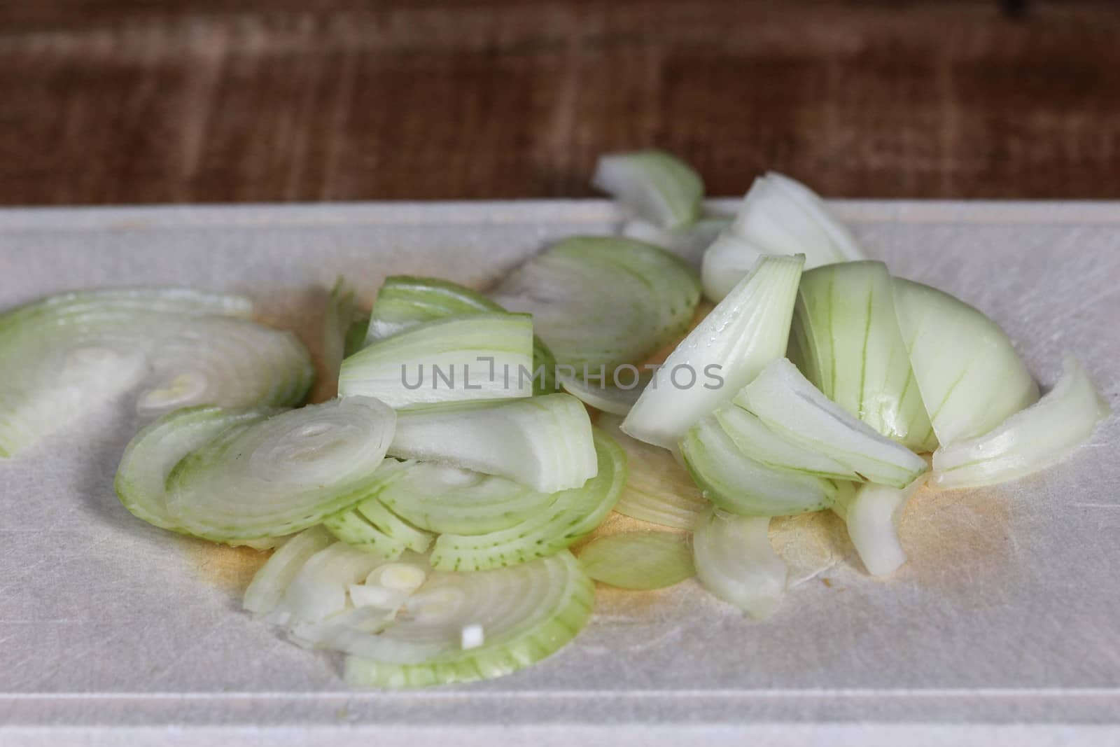 fresh healthy cutted onion on white cutting board on wooden background by michaelmeijer