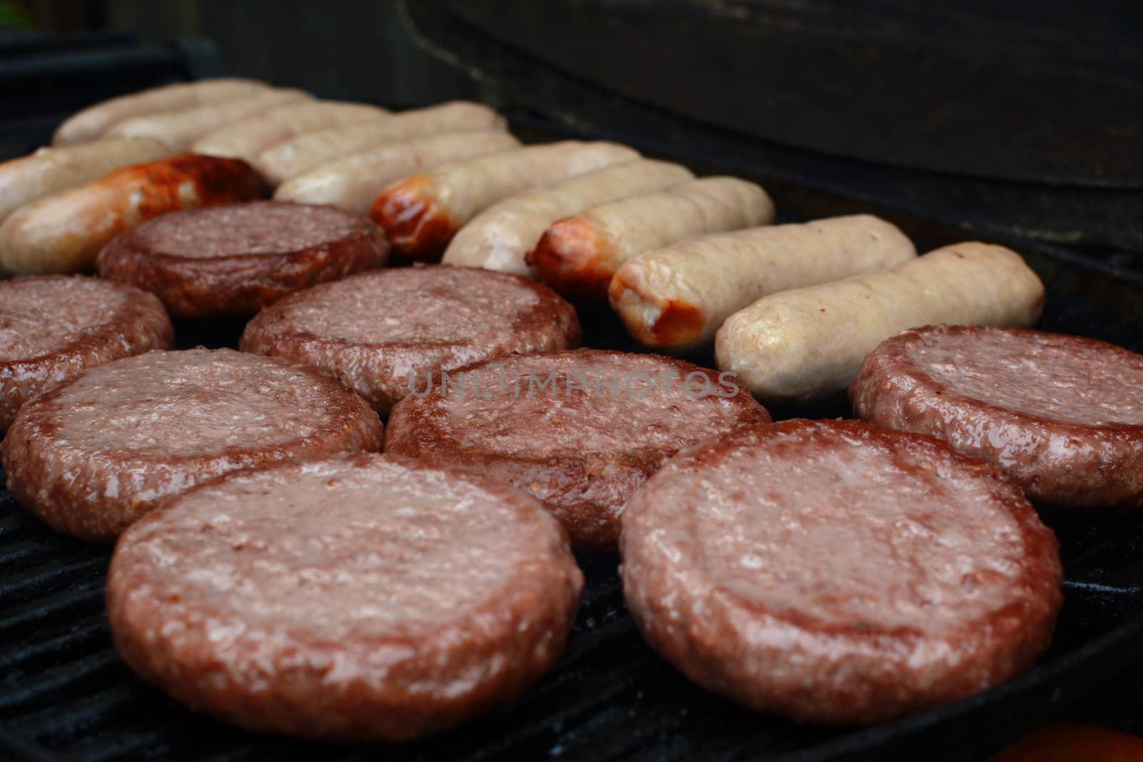 Rows of burgers and sausages starting to cook and brown on a barbecue grill