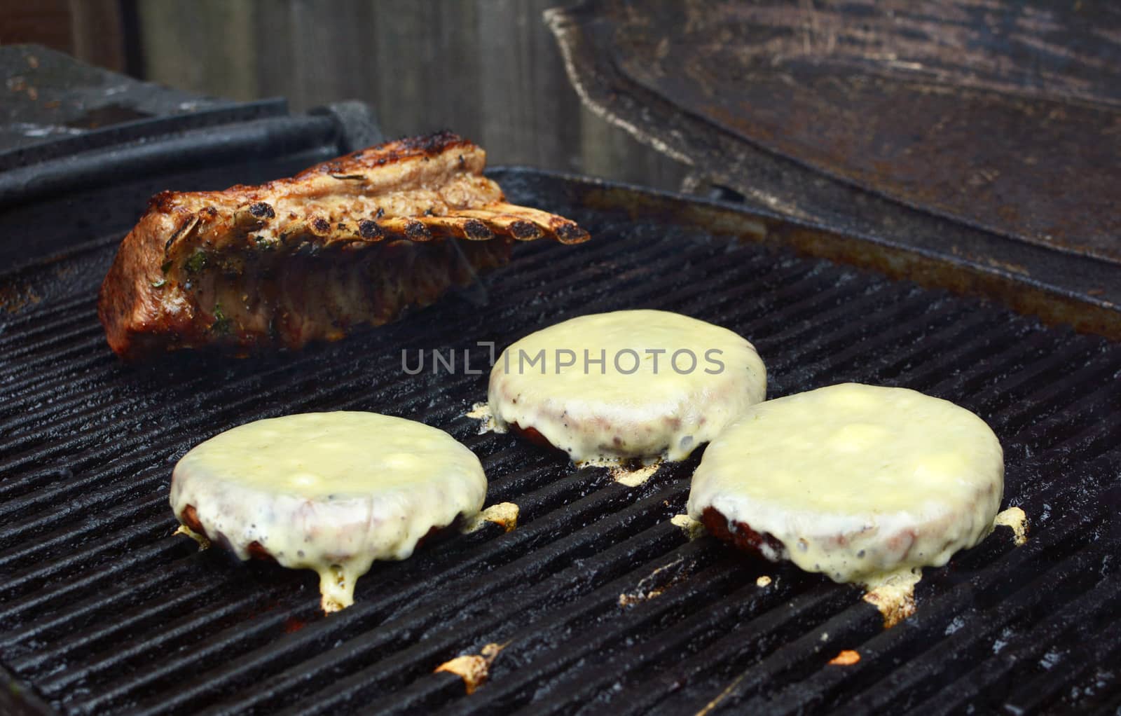Three cheeseburgers and a rack of lamb finish cooking on a barbecue grill